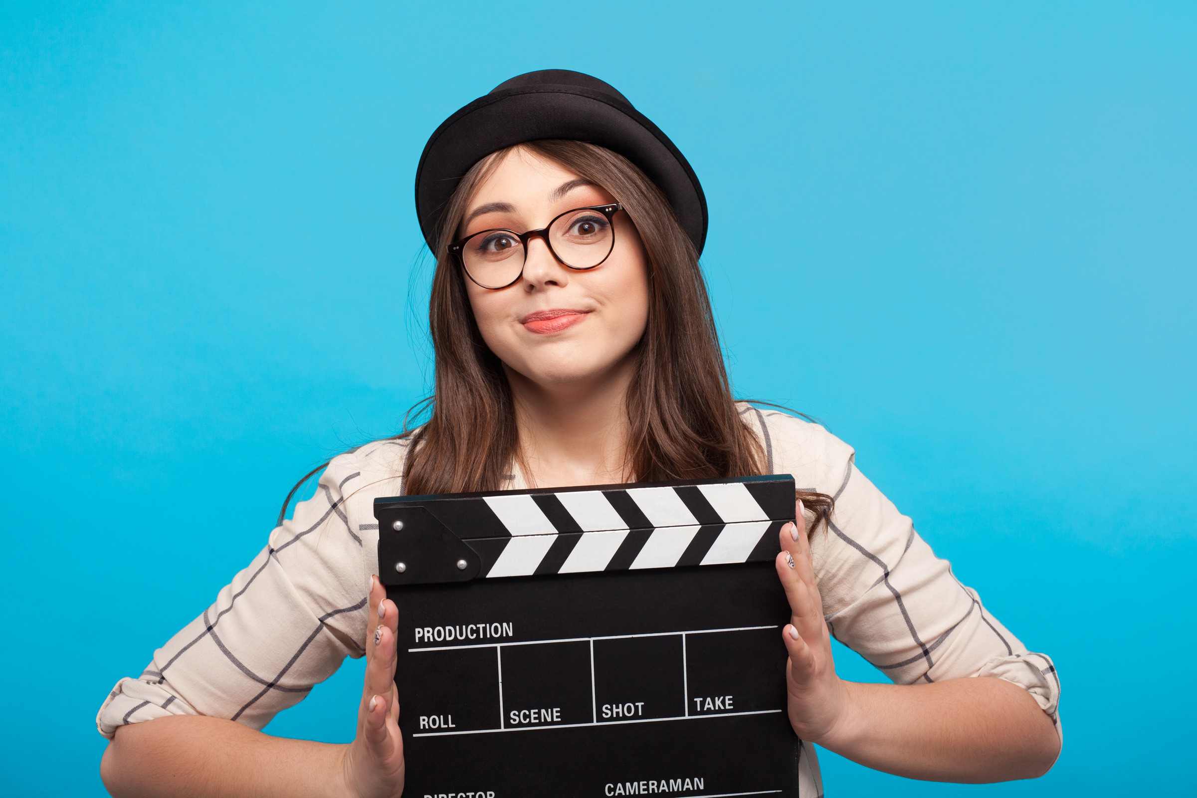 Girl holding clapperboard in front of a blue background.