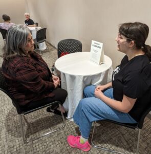 Two people are seated at a table, conversing.